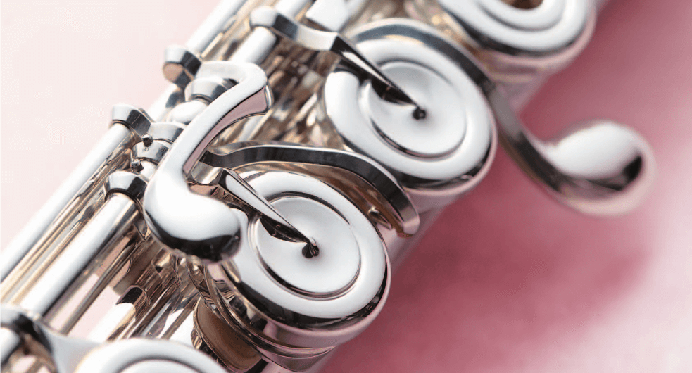 Detalle de las llaves con la forma típica de las flautas traveseras con puente francés. Fondo rosado, flauta plateada en diagonal.