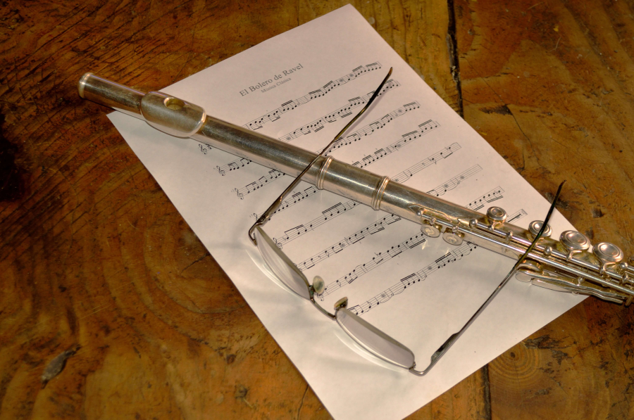Flauta en diagonal con gafas y partitura sobre mesa de madera. Aprender a tocar la flauta